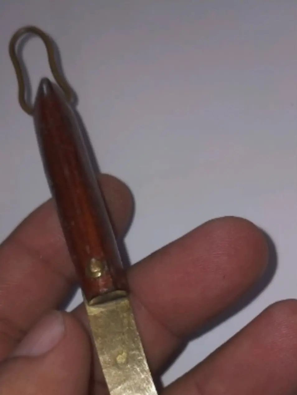 A small knife with a carved wooden handle and a brass blade, held in a hand.