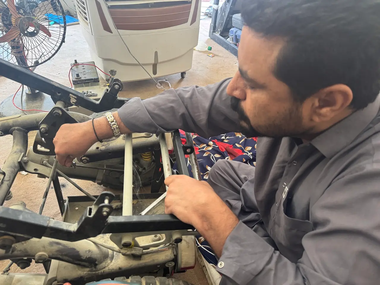 Ehsan working on a wheelchair frame in his workshop, with tools and parts laid out.
