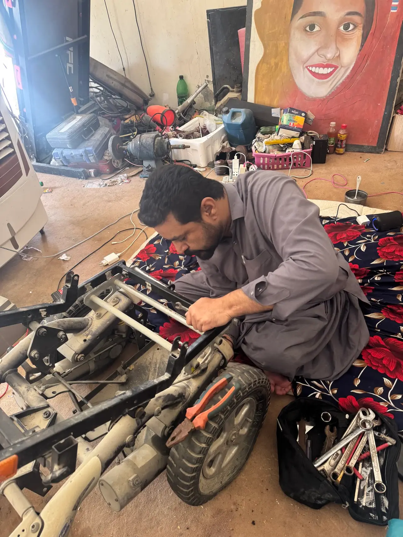 Ehsan repairing a wheelchair in his workshop in Turbat, surrounded by tools and salvaged parts.
